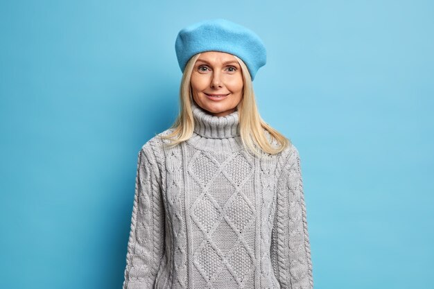 Stylish beautiful blonde woman wears french beret and knitted sweater looks happily ready for going out during autumn day.