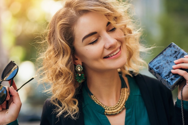 Foto gratuita elegante bella donna in jeans e giacca che cammina in strada con borsetta, stile elegante, tendenze della moda primaverile