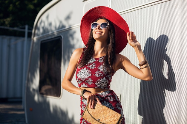 Stylish beautiful woman posing against silver trailer in tropical style outfit