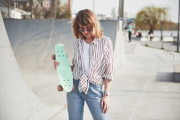 아름 다운 여름 화창한 날에 스케이트 보드와 세련 된 아름 다운 젊은 여자.