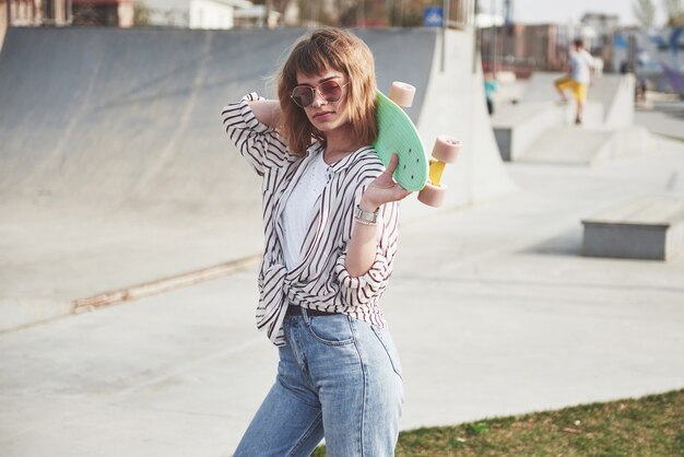 Стильная красивая молодая женщина со скейтбордом, в прекрасный летний солнечный день.