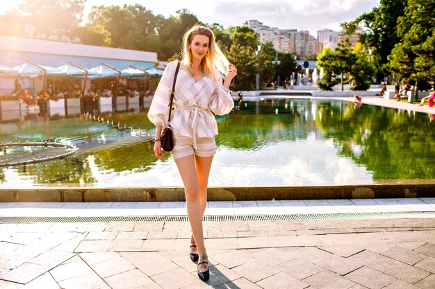 Stylish blonde woman posing on the street at sunny spring day, wearing trendy beige suit and accessories