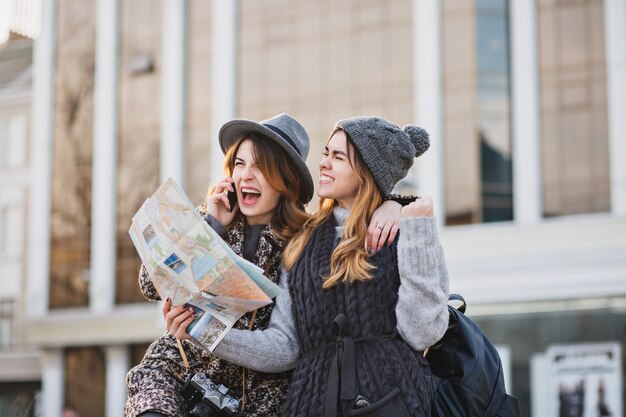 Stylish brightful image of amazing excited joyful women travelling with citymap, backpack in sunny city. Expressing positivity, lovely moments, best friends together, fashionable look.