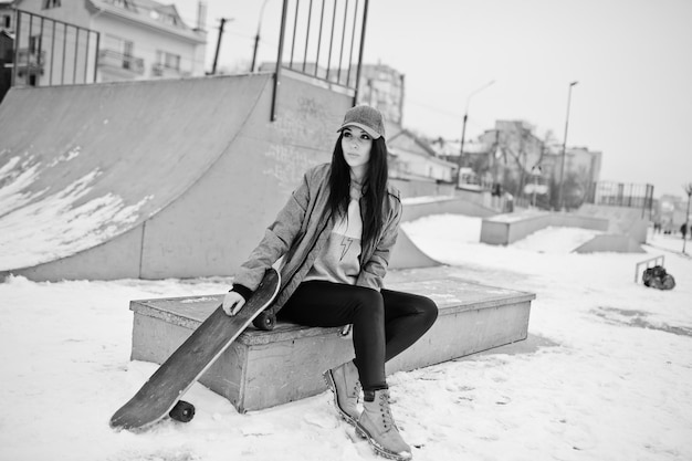 Elegante ragazza bruna in berretto grigio casual street style con skate board il giorno d'inverno