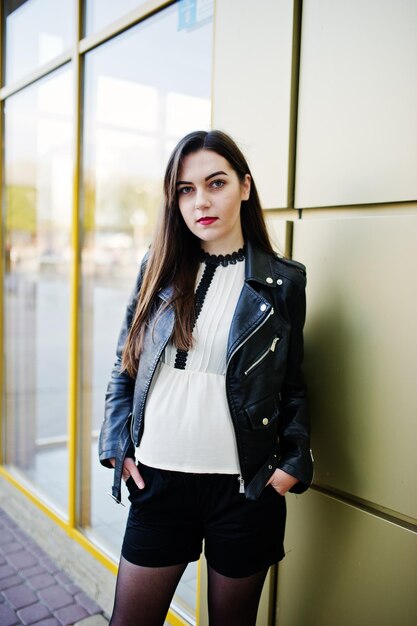 Stylish brunette girl wear on leather jacket and shorts against golden wall