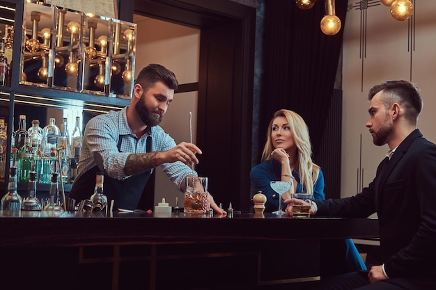 Free photo stylish brutal bartender serves an attractive couple who spend an evening on a date.