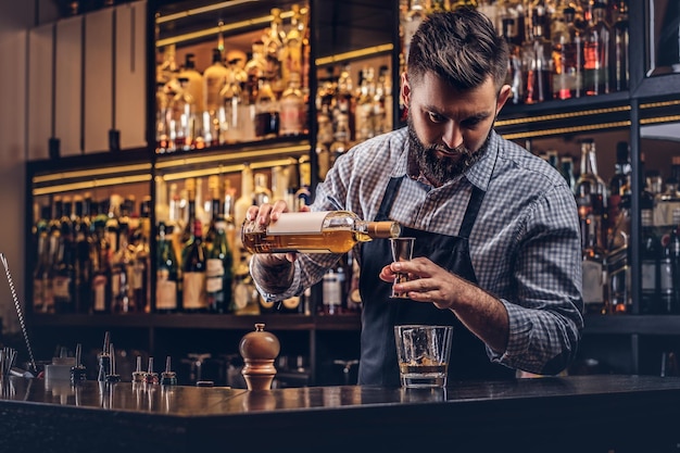 Foto gratuita elegante barista brutale in camicia e grembiule fa un cocktail sullo sfondo del bancone del bar.