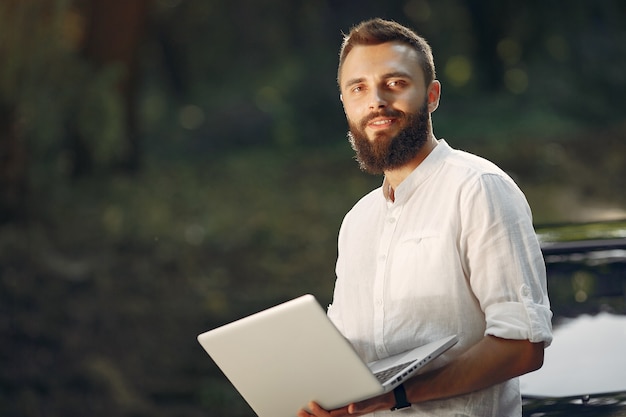 Free photo stylish businessman standing near the car and use the laptop