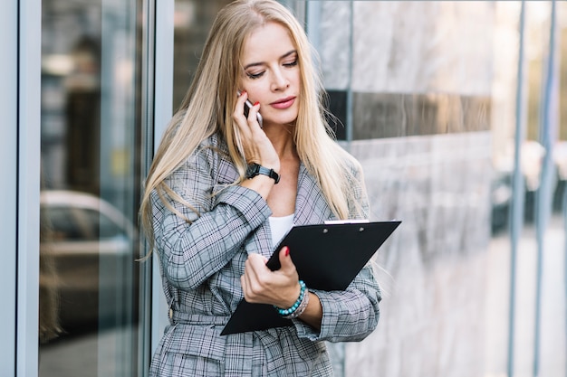 Stylish businesswoman with clipboard making phone call