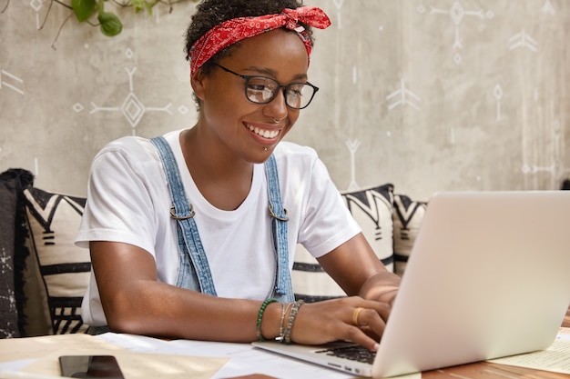 Free photo stylish businesswoman works on laptop computer in cozy coffee shop, keyboards information