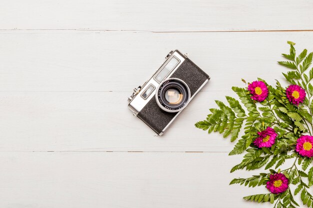 Stylish camera and pink flowers with green leaves