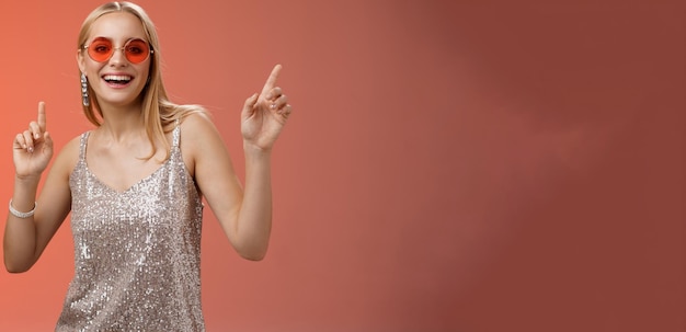 Stylish carefree fabulous young blond woman in silver dress red sunglasses having fun dancing joyful