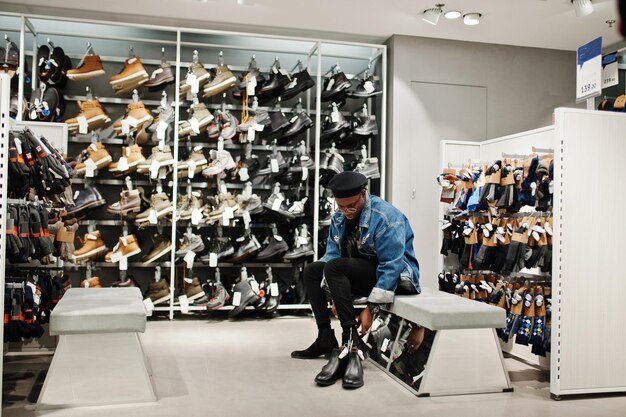 Stylish casual african american man at jeans jacket and black beret at clothes store trying new footwear