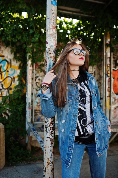 Stylish casual hipster girl in jeans wear and glasses against large graffiti wall