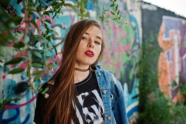 Stylish casual hipster girl in jeans wear and glasses against large graffiti wall