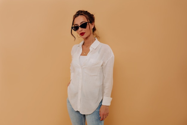 Free photo stylish caucasian young lady with dark hair and red lips posing over isolated wall