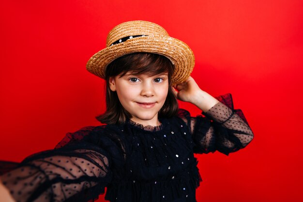自撮りを作るわらの帽子のスタイリッシュな子供。黒のドレスでかわいい女性の子供。