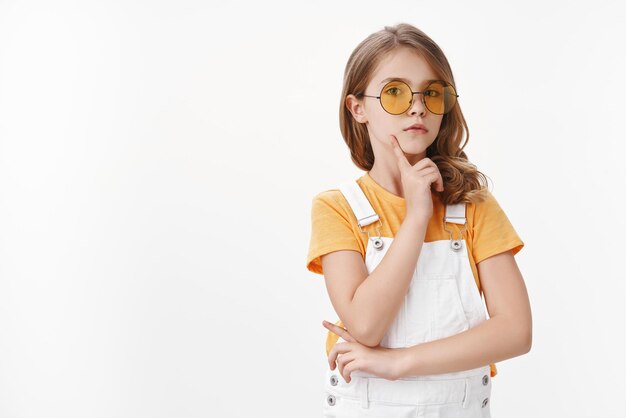 stylish confident good-looking serious little girl, charming child wear yellow sunglasses, overalls t-shirt