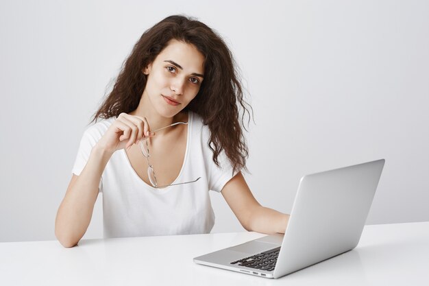 ノートパソコンで机に座りながら見ているスタイリッシュな自信を持って女性