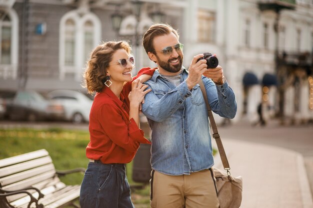 Stylish couple in love walking embracing in street on romantic trip and taking photo