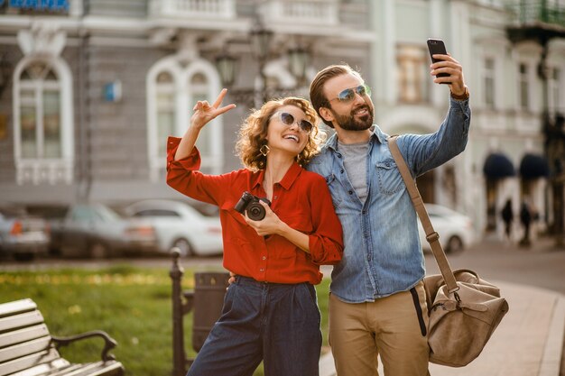 Stylish couple in love walking embracing in street on romantic trip and taking photo