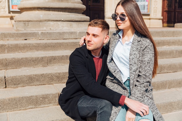 Stylish couple sitting on stairs and looking in one direction