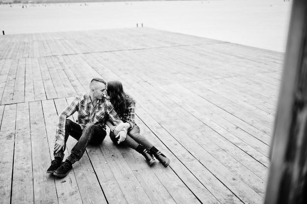 Free photo stylish couple wear on checkered shirt in love together sitting on pier