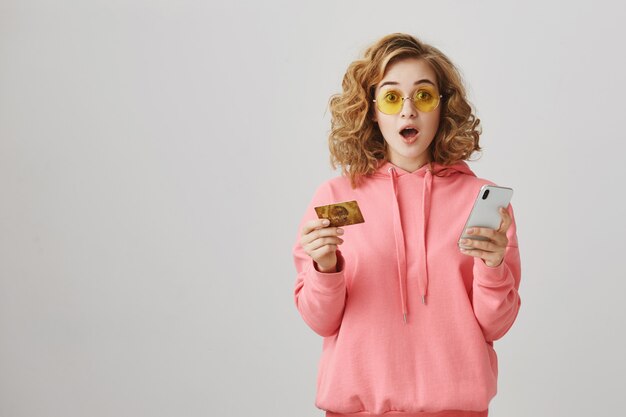 Stylish curly-haired girl shopping online, using credit card and smartphone