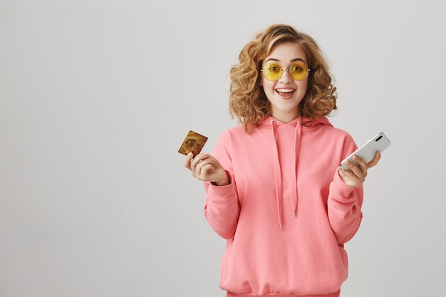 신용 카드와 스마트 폰을 사용하여 온라인 쇼핑 세련된 곱슬 머리 소녀