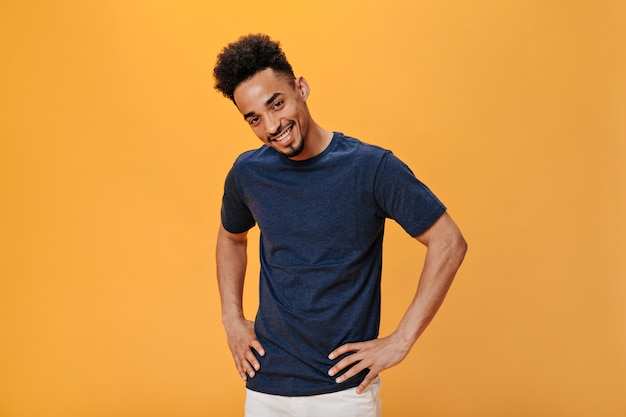 Stylish cute guy smiling and looking at camera on orange wall