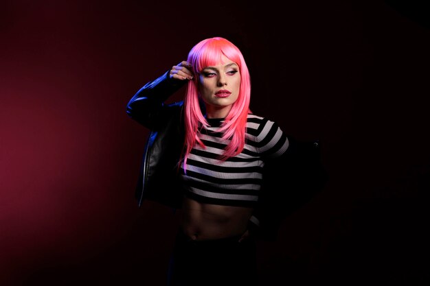 Stylish cute person doing professional pictures in studio, wearing trendy rocker leather jacket over dark background. Posing in black shadows, showing cool punk fashion trend on camera.