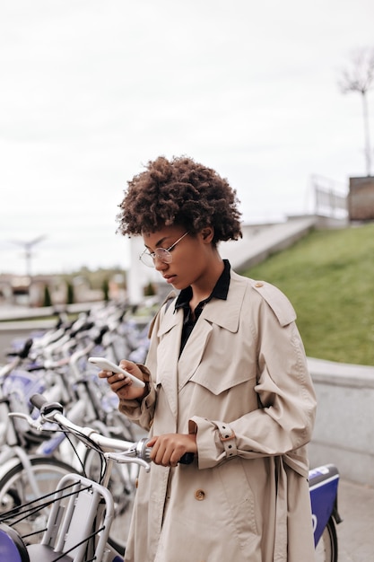 Stylish dark-skinned lady in eyeglasses holds phone