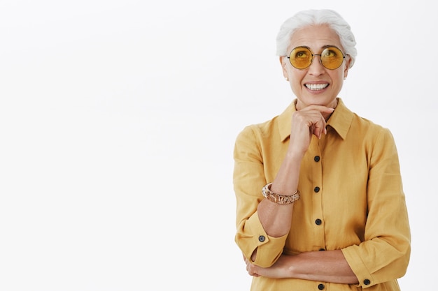 Stylish and elegant old woman in sunglasses looking up thoughtful and smiling