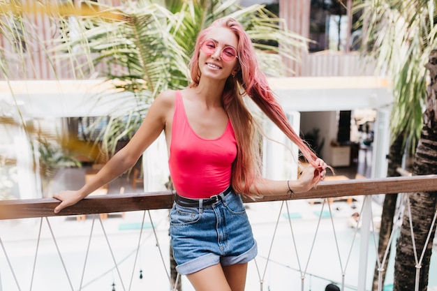 Stylish emotional woman playing with her long pink hair in summer day