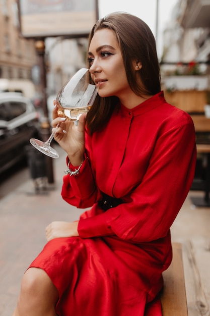 Stylish European drink tasty white wine in street restaurant. Beautiful makeup favorably emphasizes all advantages of young girl posing for portrait
