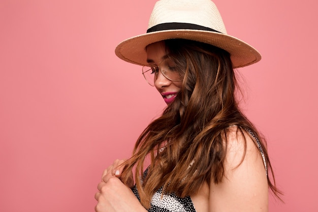 Free photo stylish european woman in hat and glasses posing over pink wall