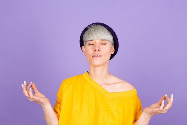 Stylish european woman on purple wall. relax and smiling doing meditation gesture with fingers