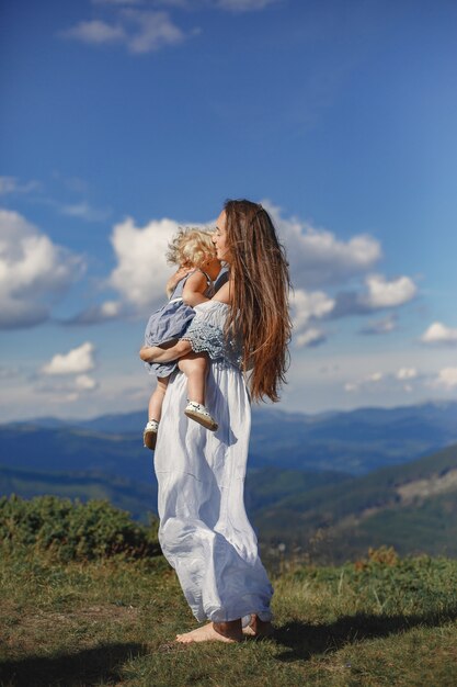 Stylish family in the mountains. Mom and daughter on a sky background. Woman in a white dress.