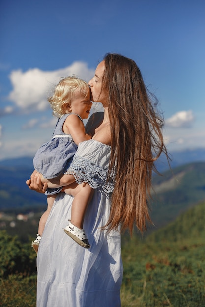 Stylish family in the mountains. Mom and daughter on a sky background. Woman in a white dress.