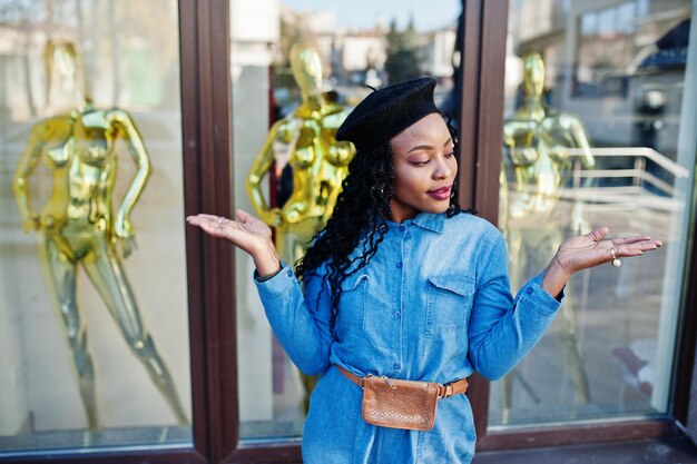 Стильные модные афроамериканки в джинсах и черном берете на фоне современного здания с тремя золотыми манекенами