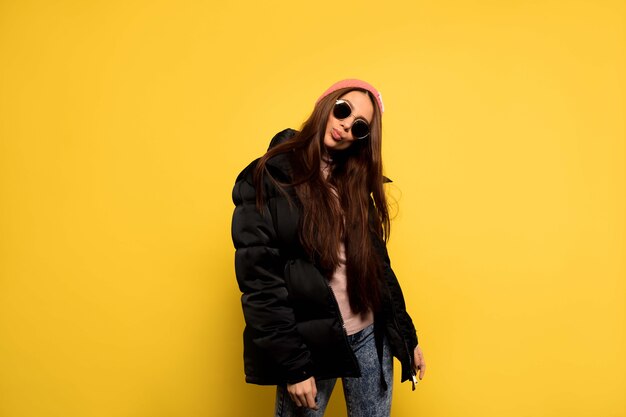 Stylish fashionable woman wearing black jacket and sunglasses and pink cap posing