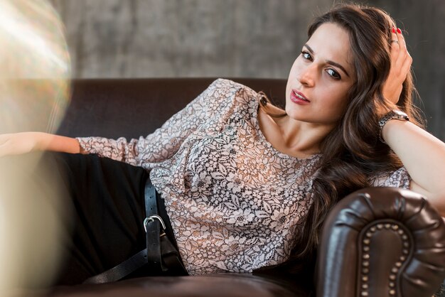 Stylish fashionable young woman lying on cozy sofa looking at camera