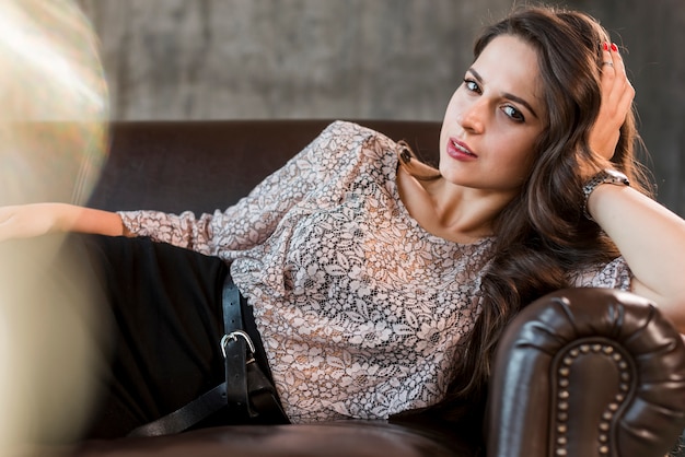 Stylish fashionable young woman lying on cozy sofa looking at camera