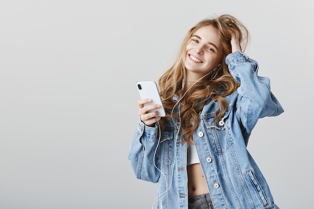 Stylish female blogger using mobile phone and listening music in earphones