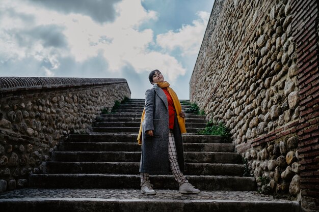 A stylish female in a coat posing in front of a stone stairs