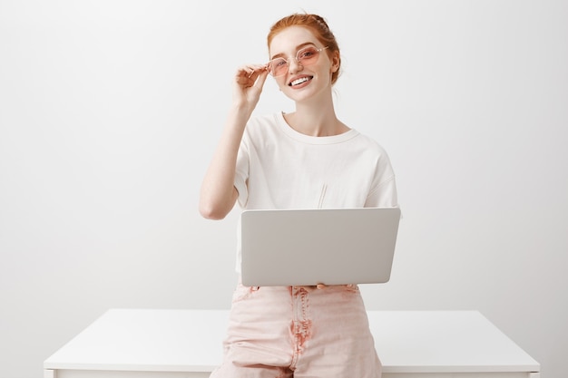 Stylish female redhead in sunglasses working with laptop