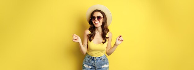 Ragazza alla moda con cappello di paglia e canotta pronta per l'estate che va in vacanza e sorridente soddisfatto standi