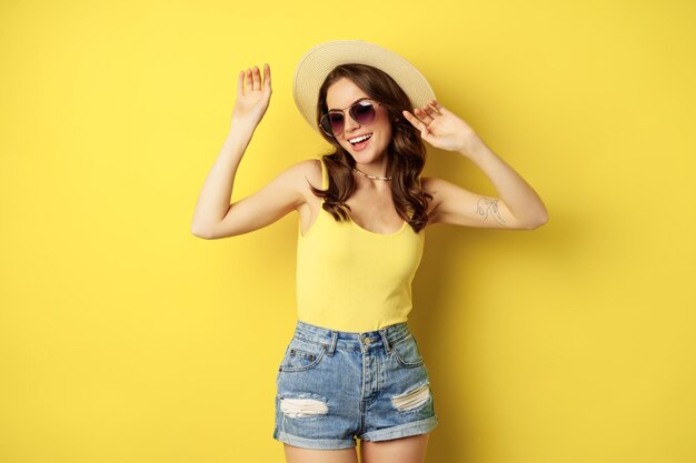 Stylish girl in straw hat and tank top ready for summer going on vacation and smiling pleased standi...