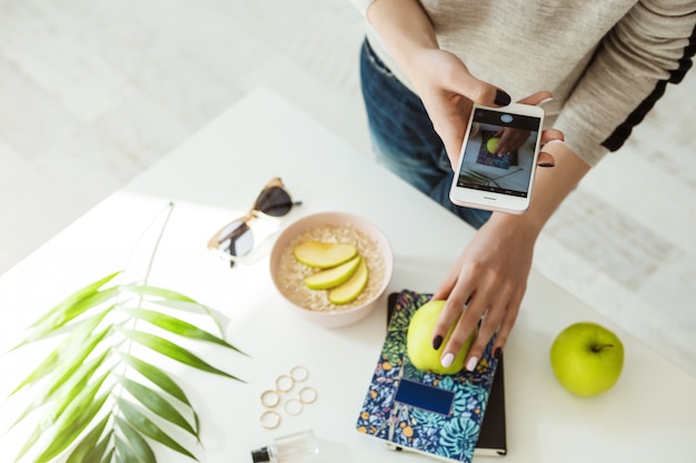 Stylish girl taking pictures with apple, notebook on whie table.