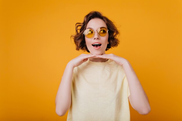 Stylish girl in trendy t-shirt posing emotionally near yellow wall